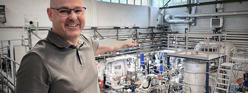 GREEN14s experimentator Björn Glaser visar på experimentuppställningen på Institutionen för Materialvetenskap på Kungliga Tekniska Högskolan. Hjärtat i processen, plasmat, skapas inuti den isolerande, stående plåttanken. Bild: GREEN14.