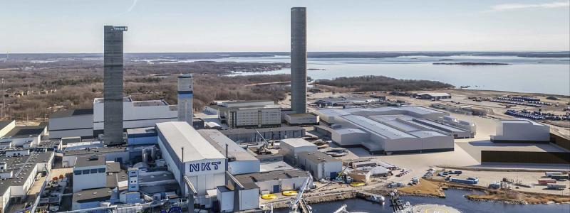 Den befintliga kabelfabriken i Karlskrona räcker inte till. Nu byggs ett nytt högt torn, men snart ska även en helt ny fabrik stå färdig. På kajen närmast fartyget ser du ett antal gula kabelrullar som ska lastas ombord för utläggning. Bild: NKT.