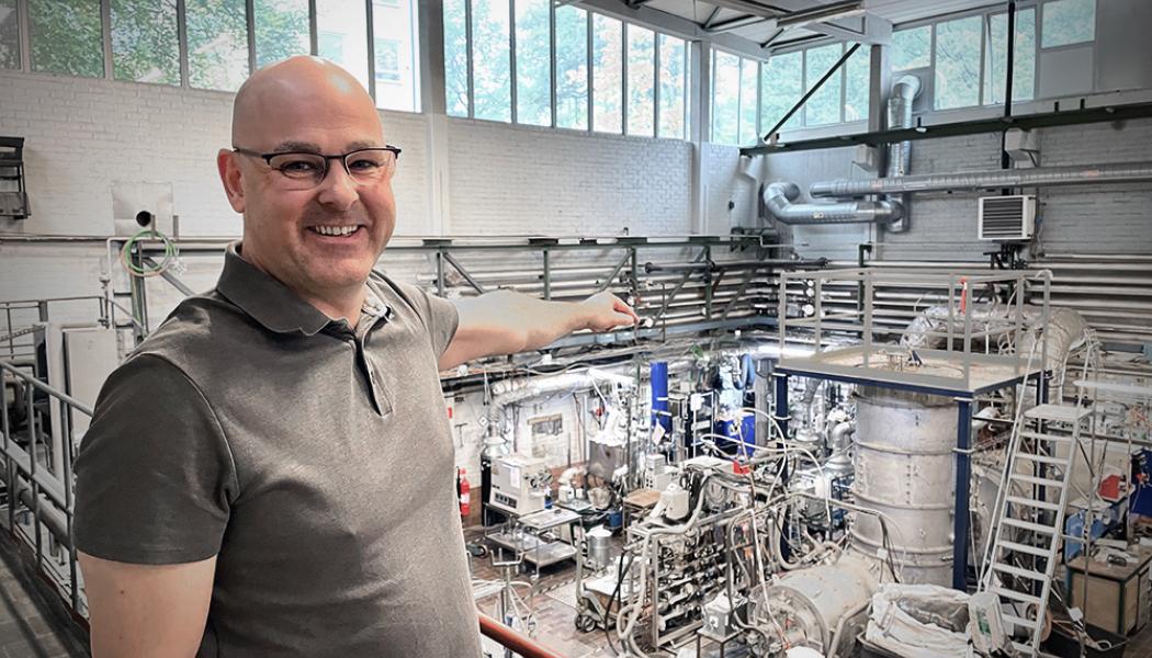 GREEN14s experimentator Björn Glaser visar på experimentuppställningen på Institutionen för Materialvetenskap på Kungliga Tekniska Högskolan. Hjärtat i processen, plasmat, skapas inuti den isolerande, stående plåttanken. Bild: GREEN14.