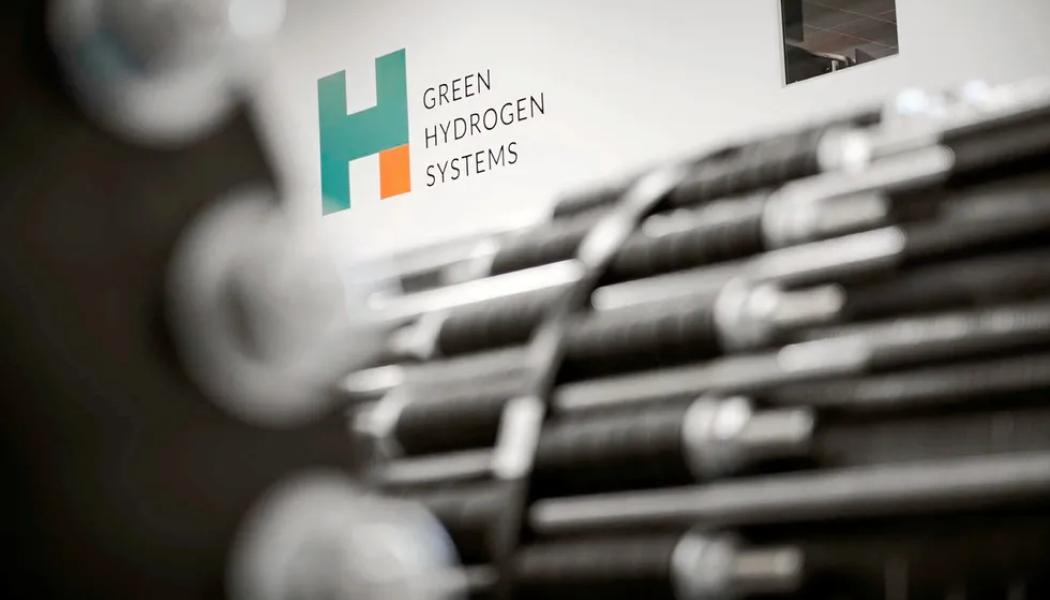 Green Hydrogen Systems' logotyp bakom elektrolysörstackar som är ur fokus. Foto: Green Hydrogen Systems.