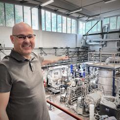 GREEN14s experimentator Björn Glaser visar på experimentuppställningen på Institutionen för Materialvetenskap på Kungliga Tekniska Högskolan. Hjärtat i processen, plasmat, skapas inuti den isolerande, stående plåttanken. Bild: GREEN14.